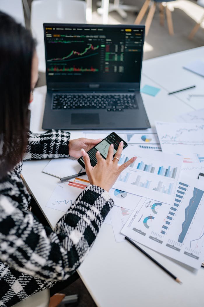 Businesswoman evaluating stock market trends using graphs and smartphone in office.